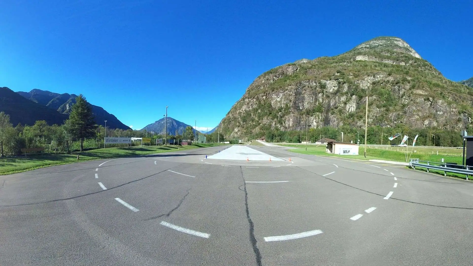 Pista di guida con segnaletica stradale e delimitazioni su un fondo asfaltato in un'area montuosa.